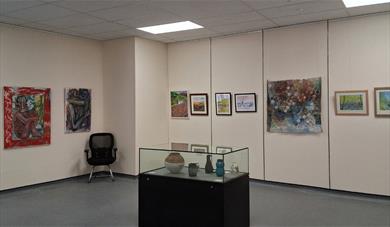 View of an exhibition gallery with artworks on the wall and a display cabinet in front
