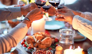 Arms and hands toasting with red wine, turkey and candles on the table.