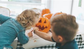 Two children cutting out a pumpkin face