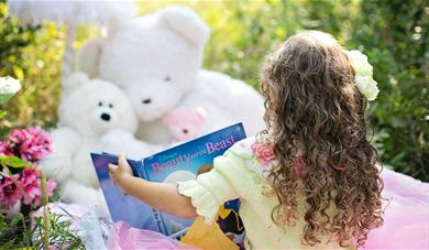 Little girl reading book to teddy bears. 