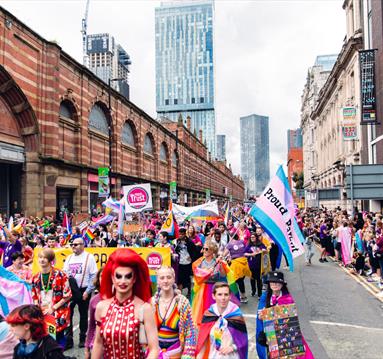 Colourful Manchester Pride Parade with people watchihng and cityscape in the background