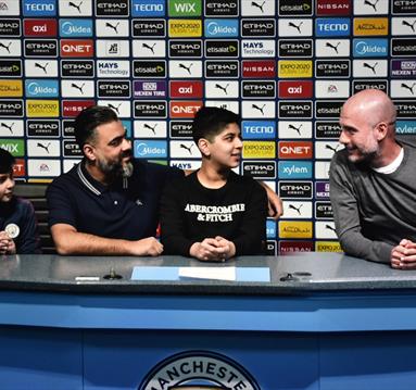 Fans sit with a virtual Pep Guardiola at the Manchester City Stadium Tour