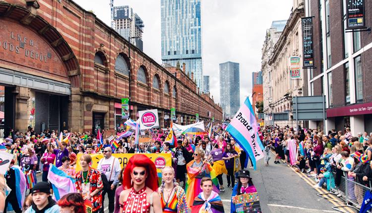 Colourful Manchester Pride Parade with people watchihng and cityscape in the background