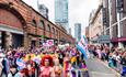 Colourful Manchester Pride Parade with people watchihng and cityscape in the background