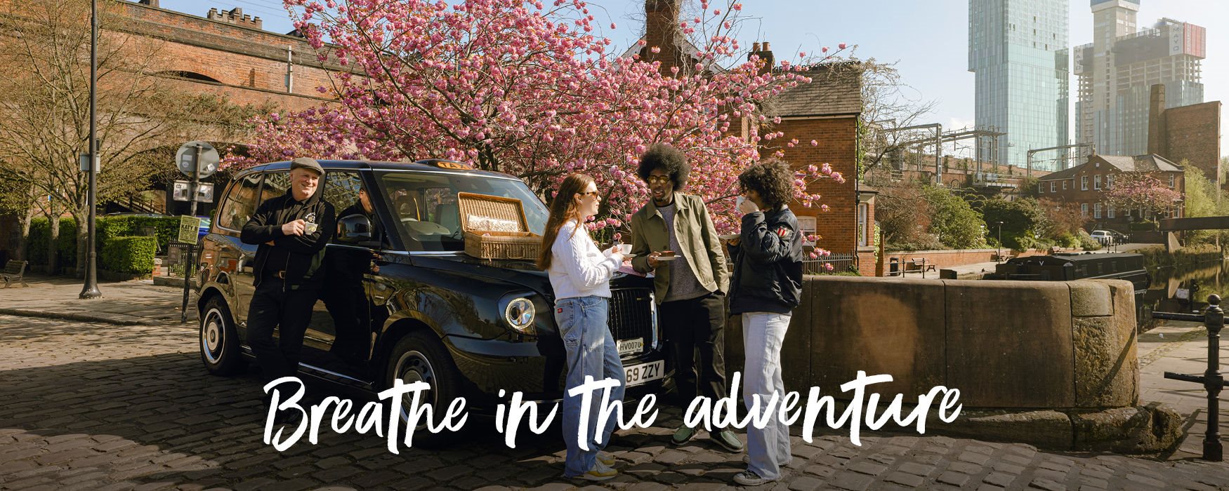 Friends enjoying taxi tour guide in Manchester on a cobbled street with cherry blossom tree in the background