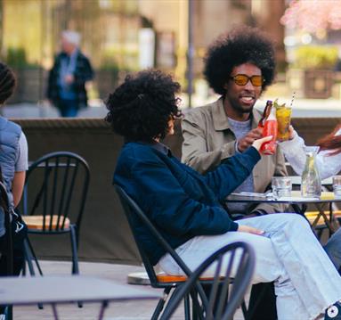 Group of friends with drinks sat at a table outside in the sun in Manchester