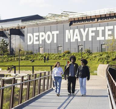 People walking in park with Depot Mayfield behind them