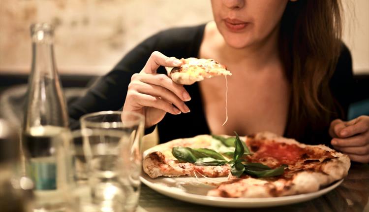 Woman Holds Sliced Pizza Seats by Table With Glass