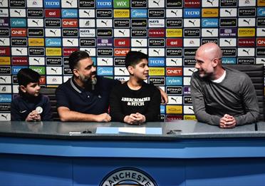 Fans sit with a virtual Pep Guardiola at the Manchester City Stadium Tour