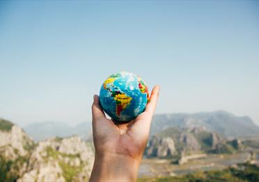 Person Holding World Globe Facing Mountain