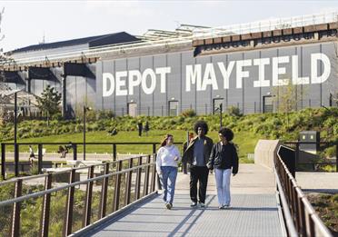 People walking in park with Depot Mayfield behind them