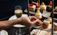 Person reaching for cake from an afternoon tea platter with champagne