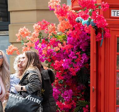 3 people taking a selfie outside a red telephone box filled with flowers