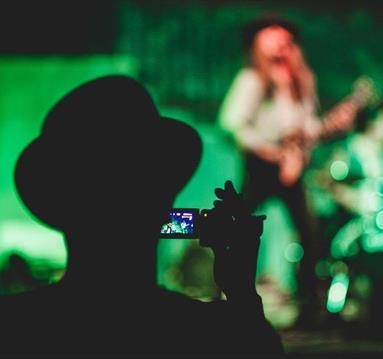 Person recording video of a person playing guitar onstage