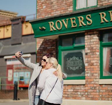 2 people posing for a photo outside of Rovers Return on the Coronation Street tour in Manchester