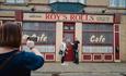 2 people posing for a photo outside of Roy's Rolls on the Coronation Street tour in Manchester