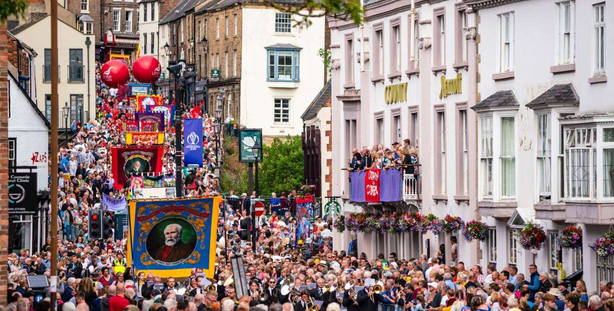 Crowds pass under the balcony of the County Hotel and along Old Elvet at the 2019 Durham Miners' Gala