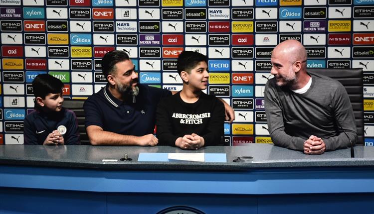 Fans sit with a virtual Pep Guardiola at the Manchester City Stadium Tour