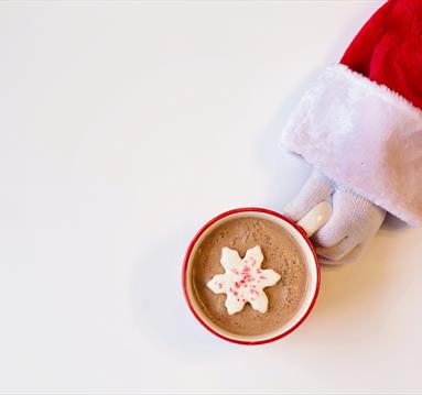 Mug of Chocolate Drink With Snowflake-Shaped Cookie On Top Held By A Person In Santa Suit