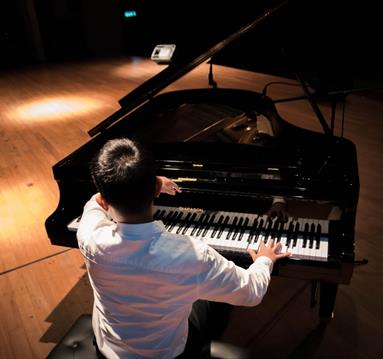 Back View Photo of a Man Playing a Black Grand Piano