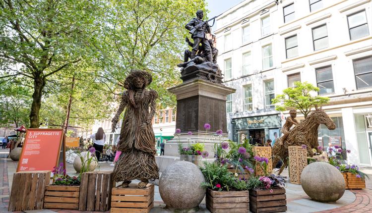 Wooden sculptures around a monument in manchester with floral displays