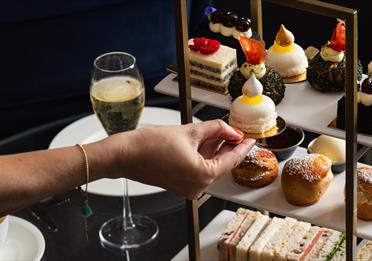 Person reaching for cake from an afternoon tea platter with champagne