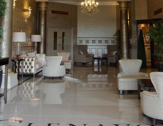 Image of the entrance hall with shiny tiled floors, cream armchairs, gold metallic columns and patterned wallpaper