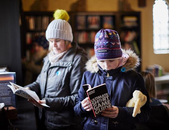 Two people with coats and hats on looking at books
