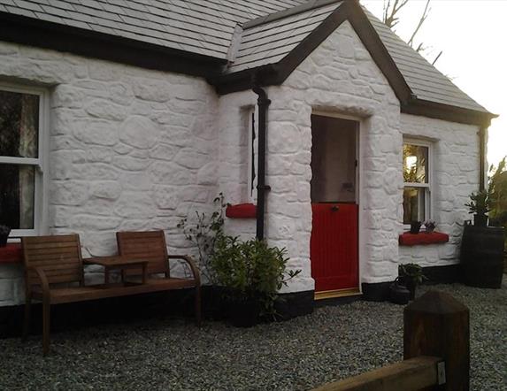 Outside view of cottage with red door and wooden chairs at front