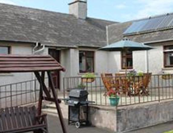 Outside image of house with accessibility ramp, table and chairs, wooden swing chair