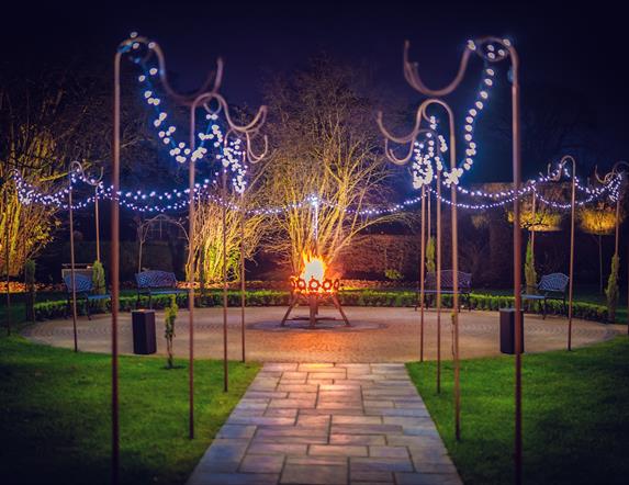 Paved path leading to circular patio with fairy lights and fire pit.