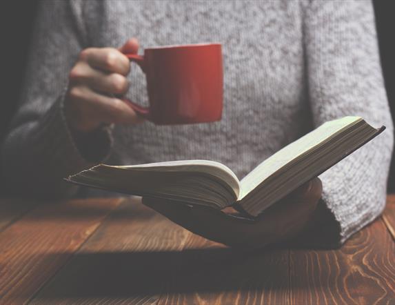 Image of someone holding an open book and a red mug