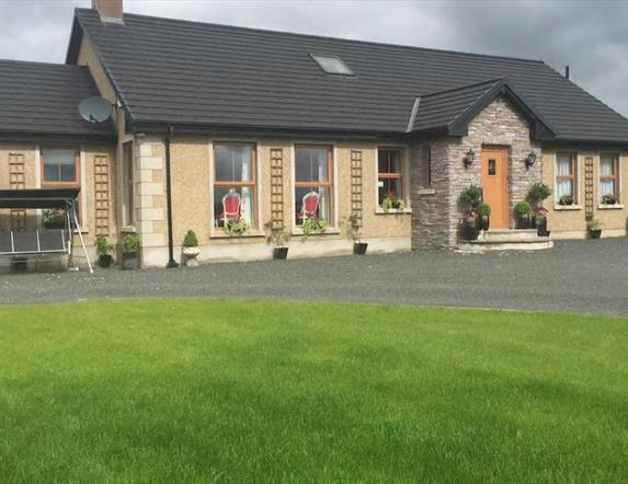 outside view of cottage with swing chair and grass garden area in image