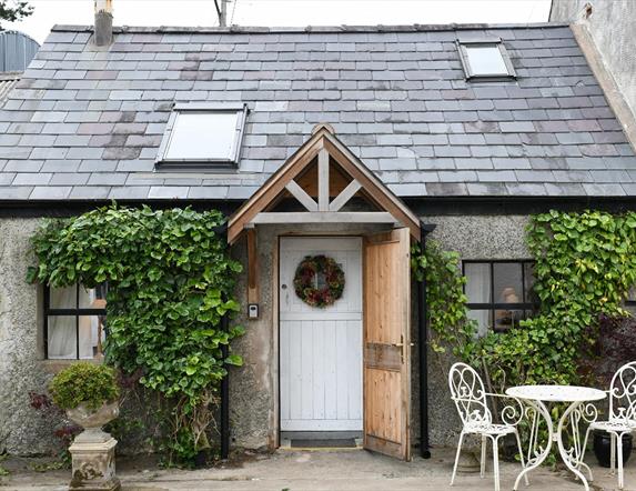 Outside view of Milk House with greenery on the walls and outside table and 2 chairs