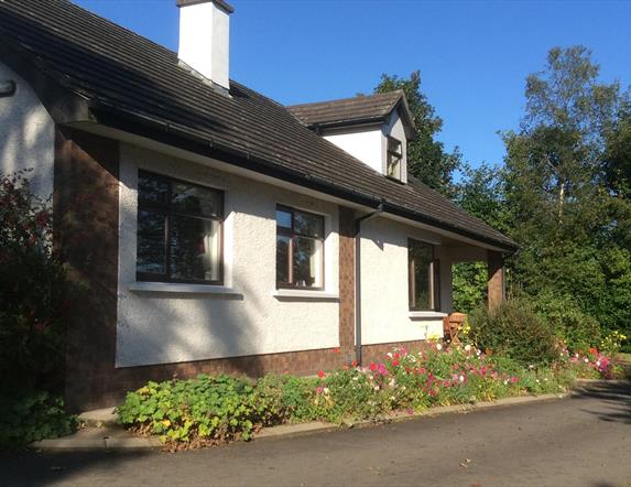 Image of a cream bungalow with flower beds and tress surrounding it