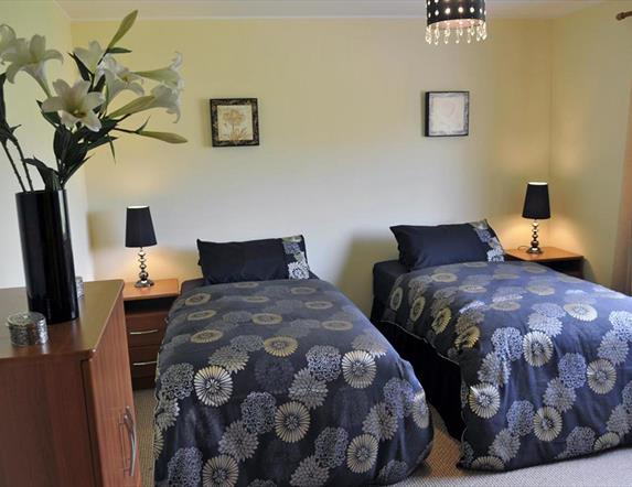 Twin bedroom with 2 single beds with bedside lockers and bunch of flowers in image