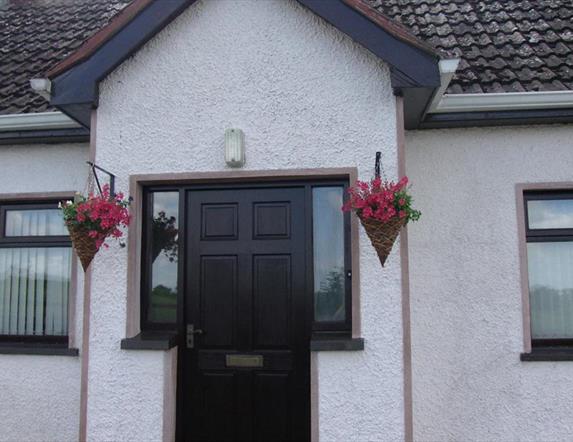 Image of the front of a white bungalow with flower baskets hanging on either side of the door