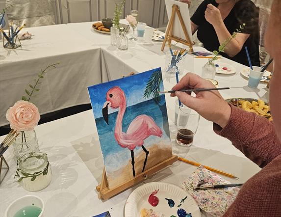H shaped table with people painting a pink flamingo