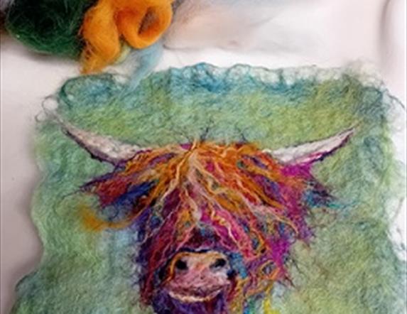 A small piece of felt craft using orange and purple hews to create an image of a highland cow's head against a moss green background.