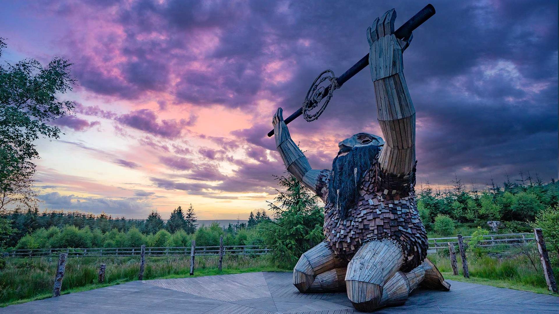 A giant wooden sculpture kneeling in the forest with the sun setting