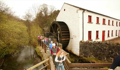 A group of people walking past the water wheel at Wellbrooke 