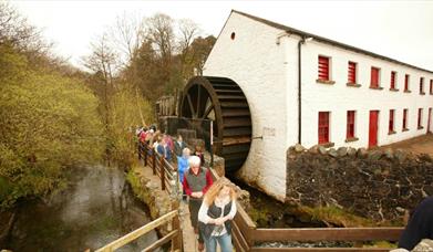 A group of people walking past the water wheel at Wellbrooke