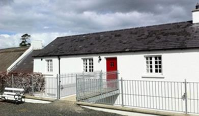 Outside of cottage with white exterior and red door 