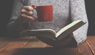 Image of someone holding an open book and a red mug