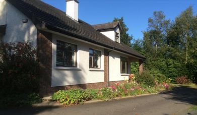 Image of a cream bungalow with flower beds and tress surrounding it