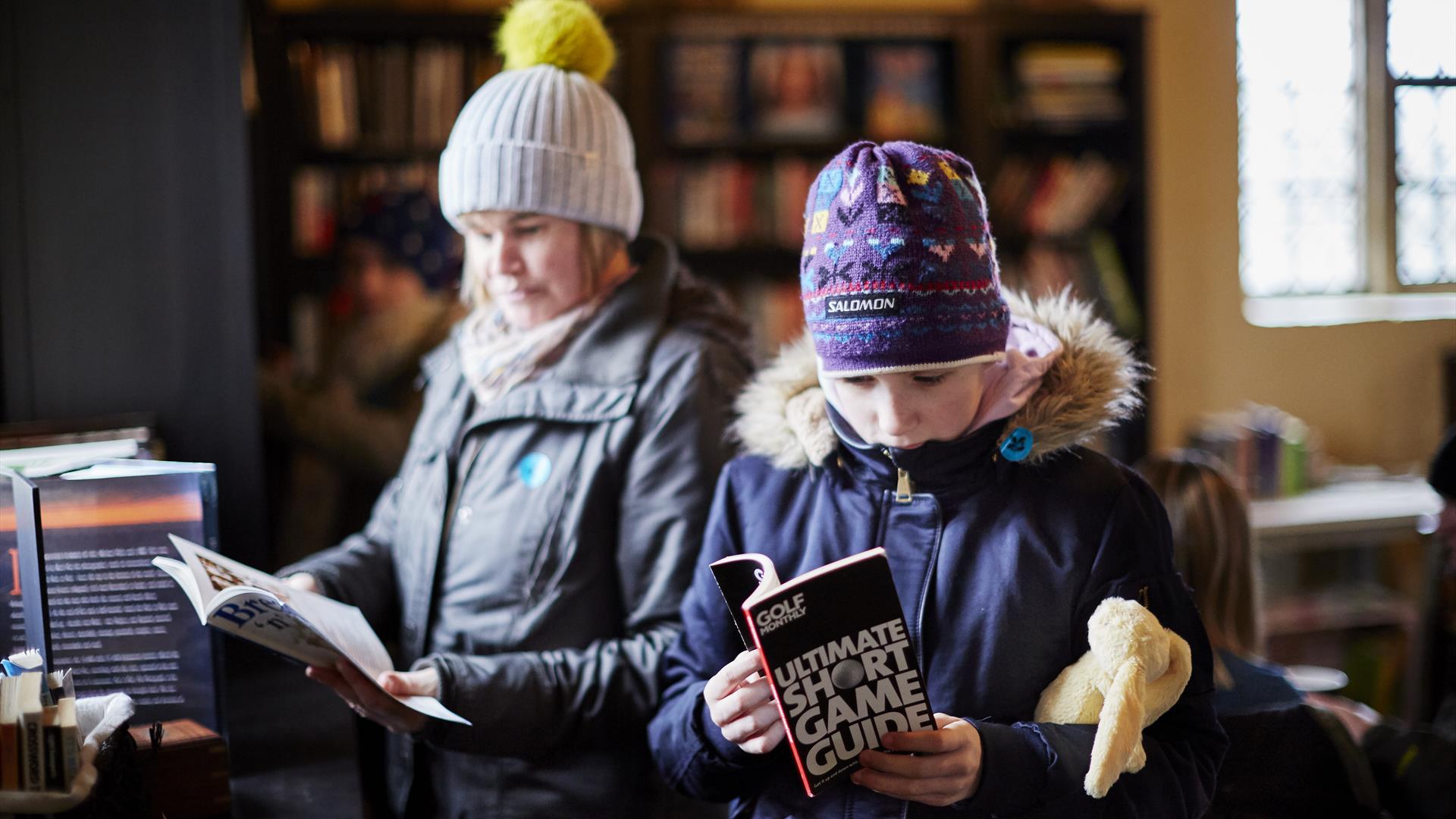 Two people with coats and hats on looking at books