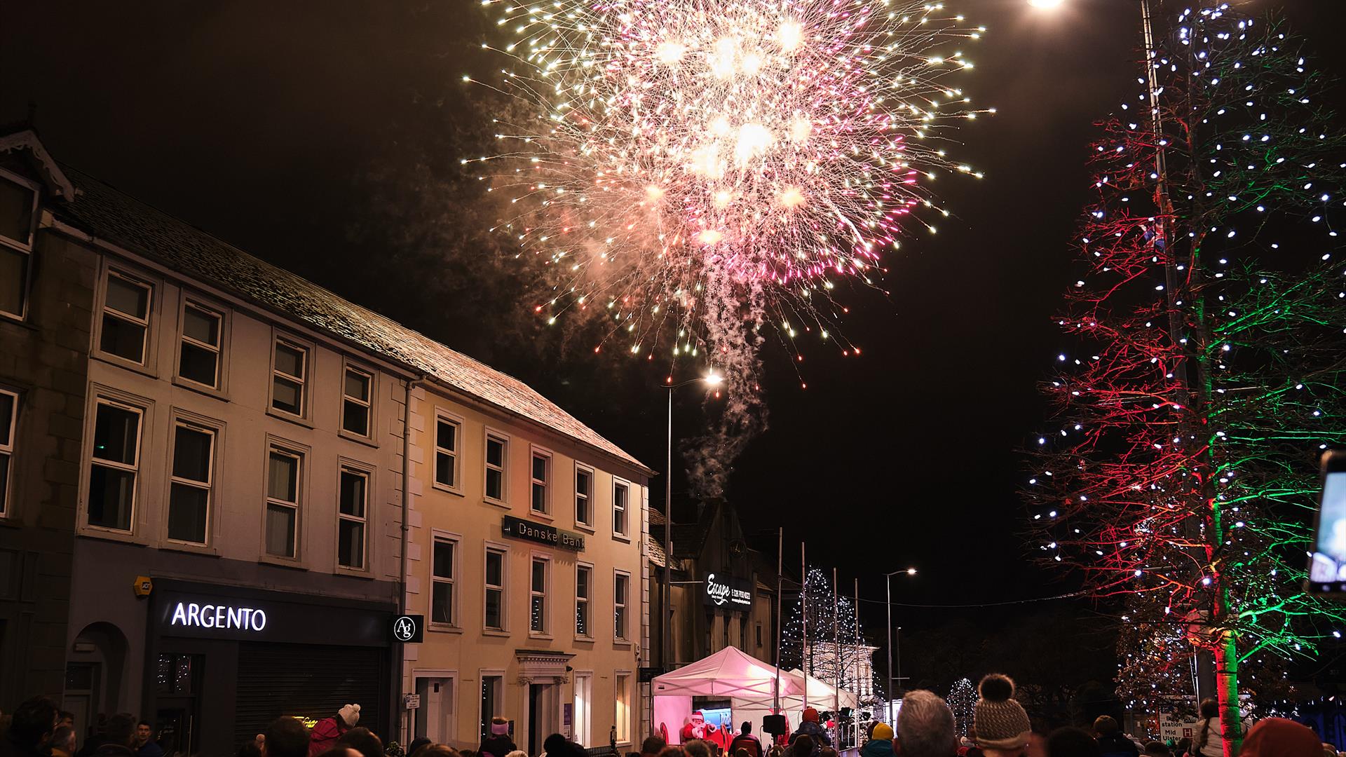 Multi-coloured fireworks are exploding in the sky over the roof of buildings on Magherafelt's Main Street