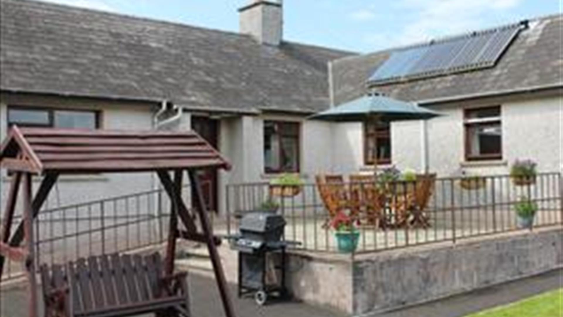 Outside image of house with accessibility ramp, table and chairs, wooden swing chair