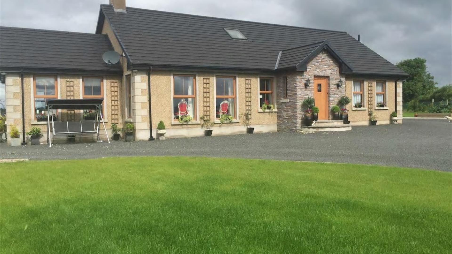 outside view of cottage with swing chair and grass garden area in image