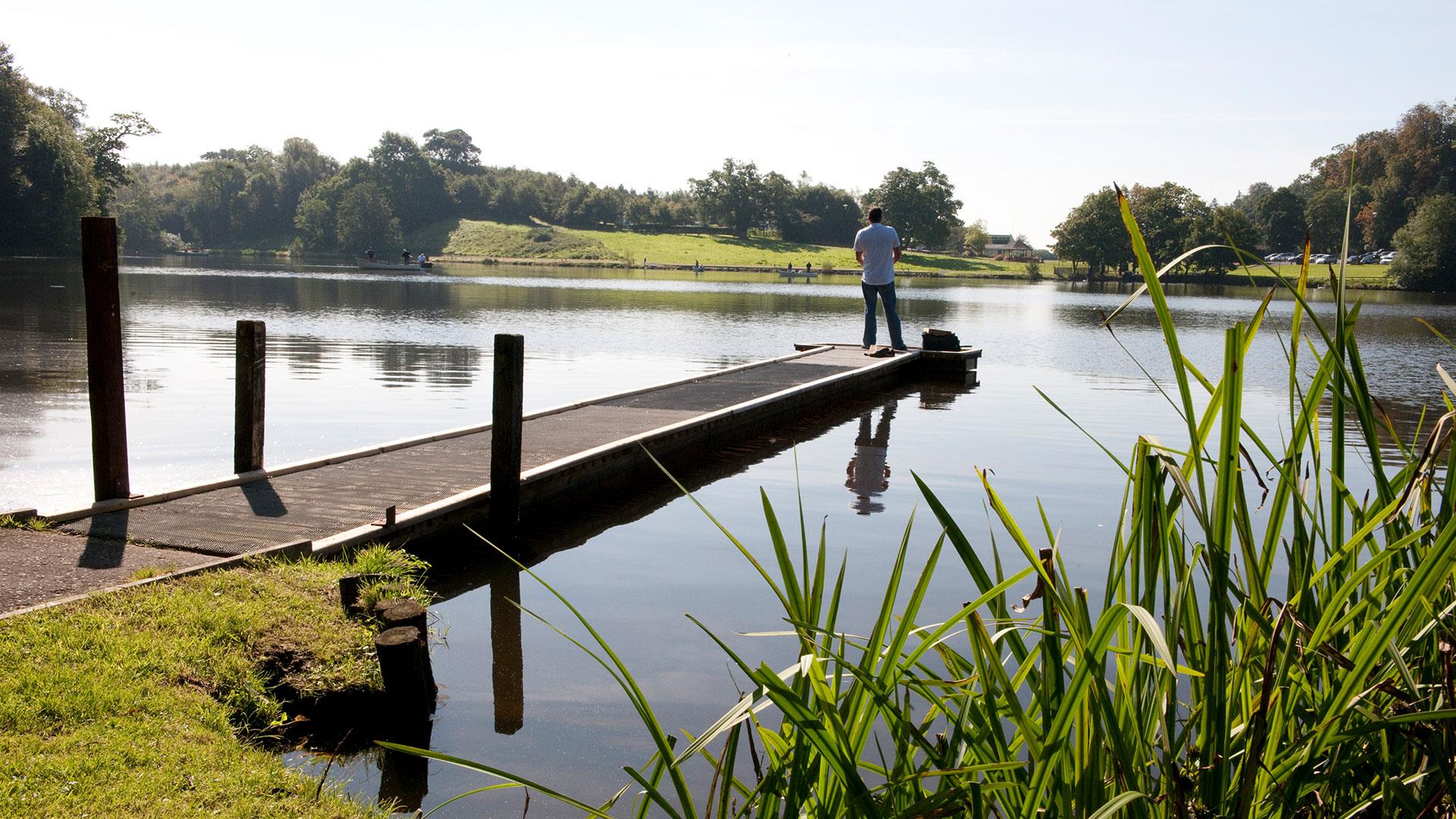 A man standing fishing on the jetty at Dungannon park lake